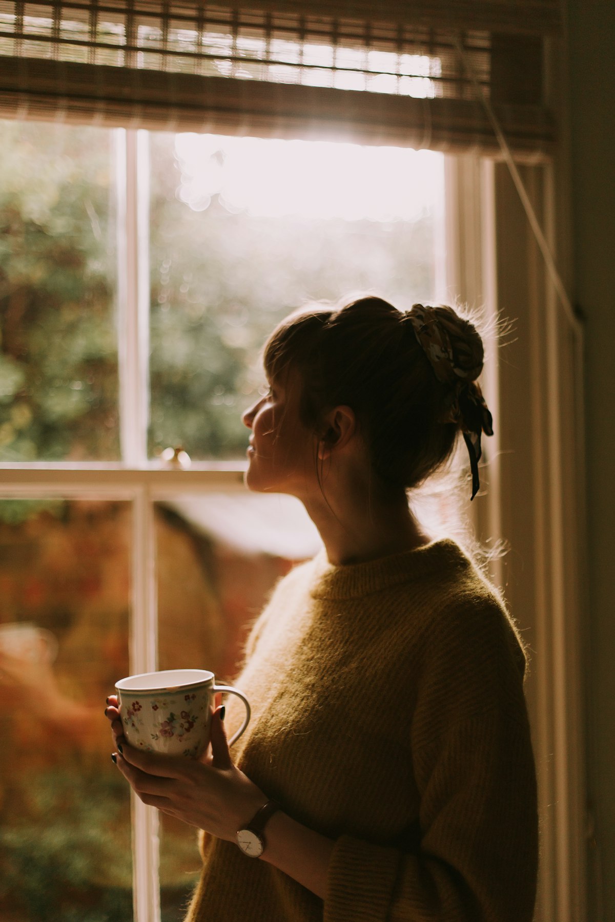 A person pausing with a warm cup of tea by a window